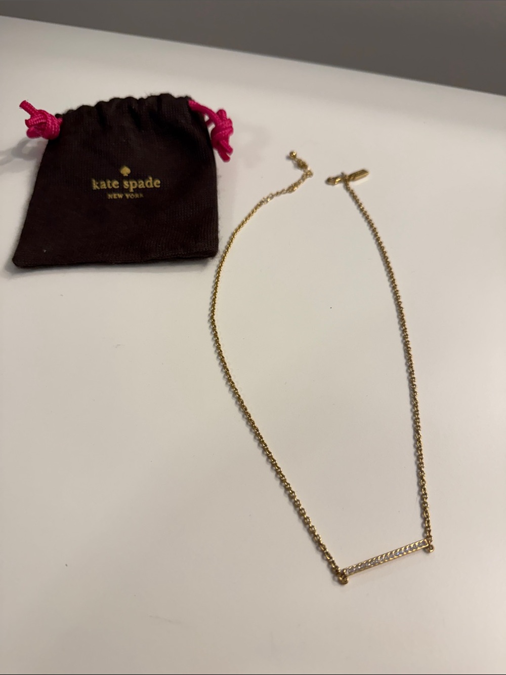 kate spade gold bar pendant necklace with brown pouch and pink drawstrings